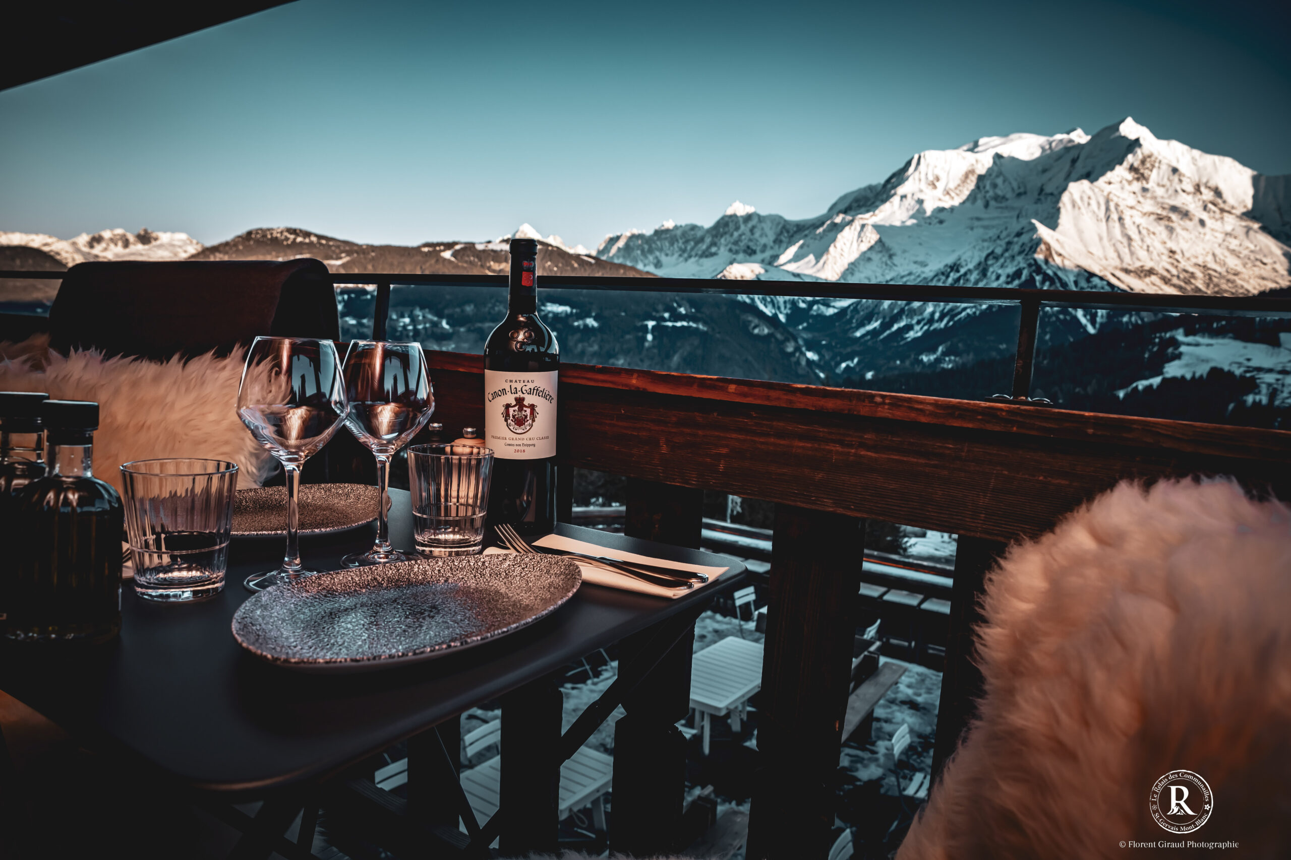 Terrasse en bois entourée de montagnes enneigées avec bouteille de vin